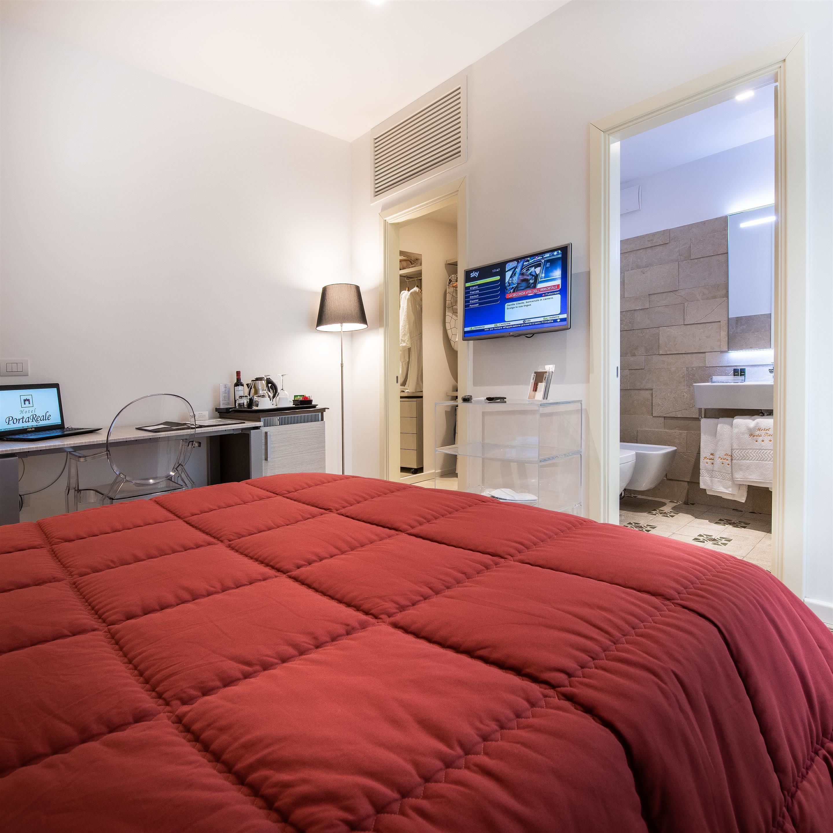 Una habitación de hotel con cama, escritorio con una computadora portátil, televisor y baño con ducha e inodoro.
