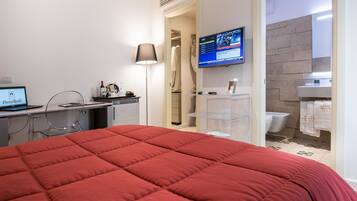 Una habitación de hotel con cama, escritorio con una computadora portátil, televisor y baño con ducha e inodoro.