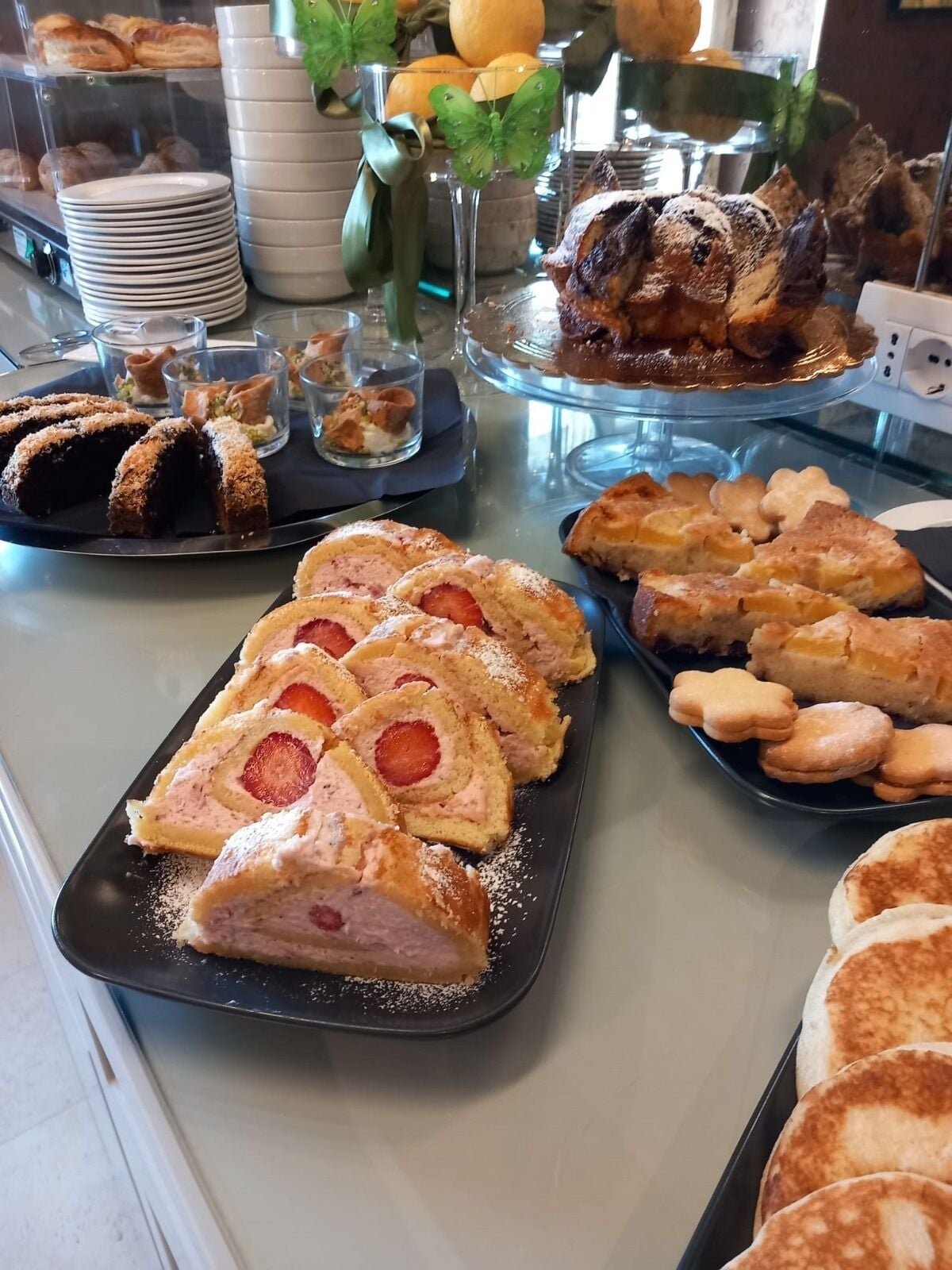 Un buffet con diverse paste e dolci, tra cui un rotolo alla fragola e altri prodotti da forno.