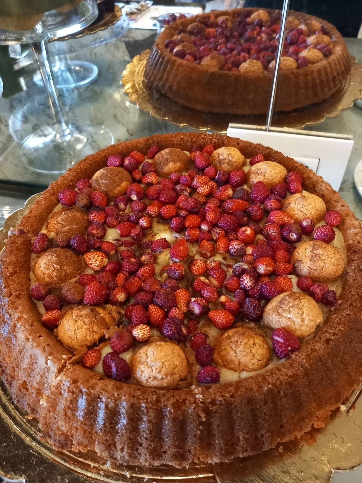 A round cake with strawberries and cream on a glass display.