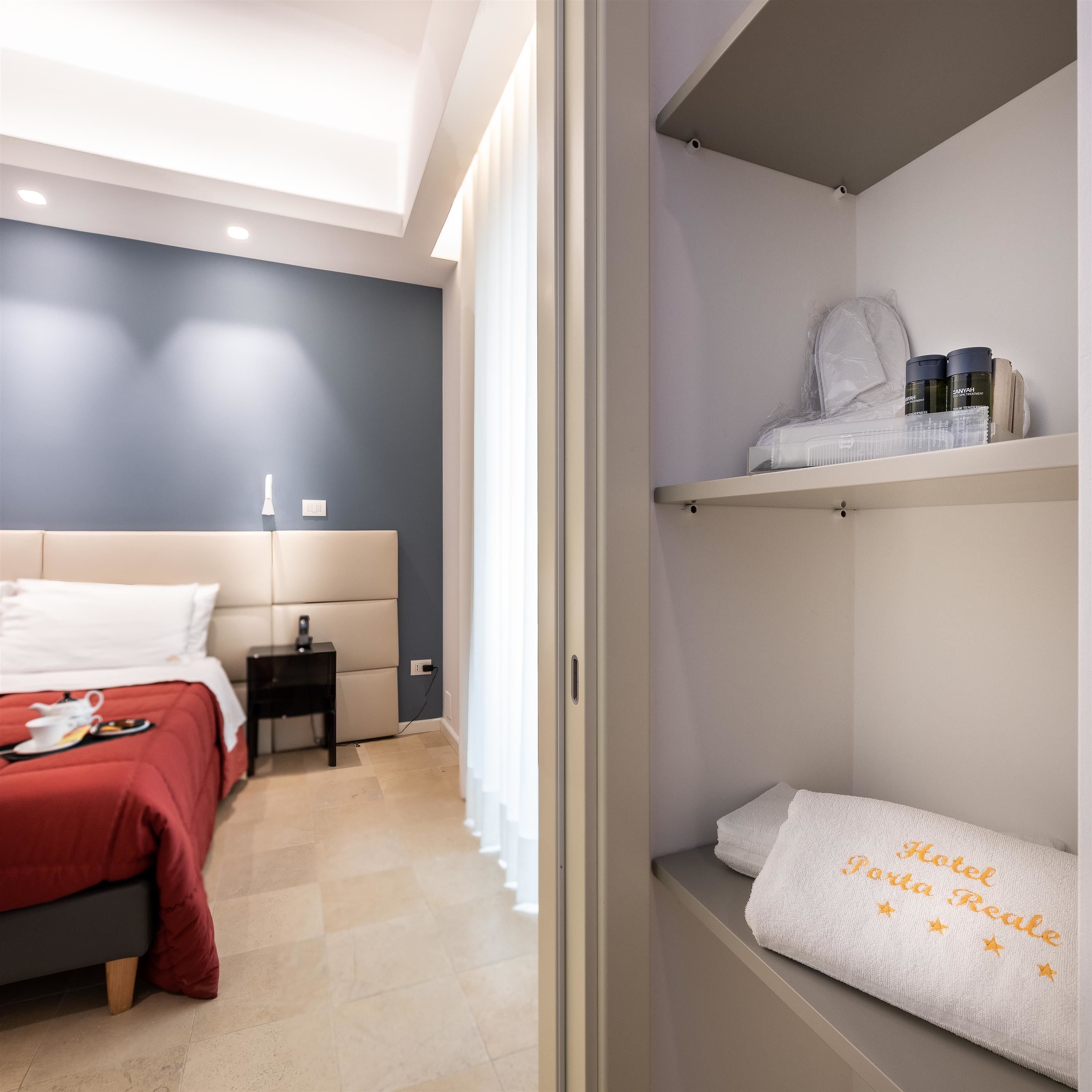 Quarto de hotel com cama, mesa de cabeceira e um armário com produtos de higiene pessoal.