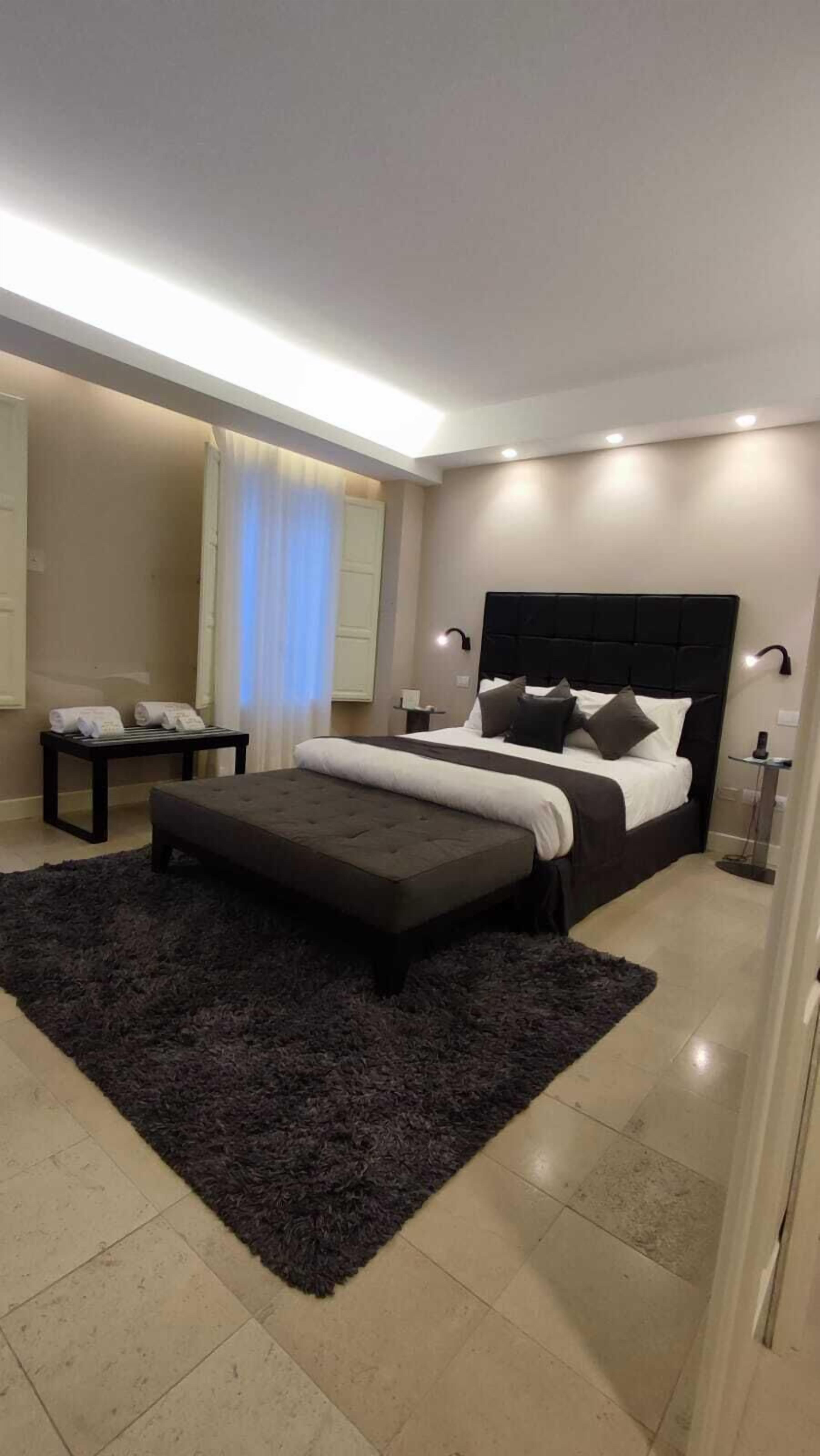 A modern bedroom with a large bed, a dark rug, and a bedside table with lamps.