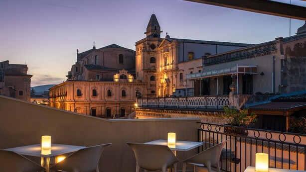 A rooftop terrace with tables and chairs, overlooking historic buildings and a church.