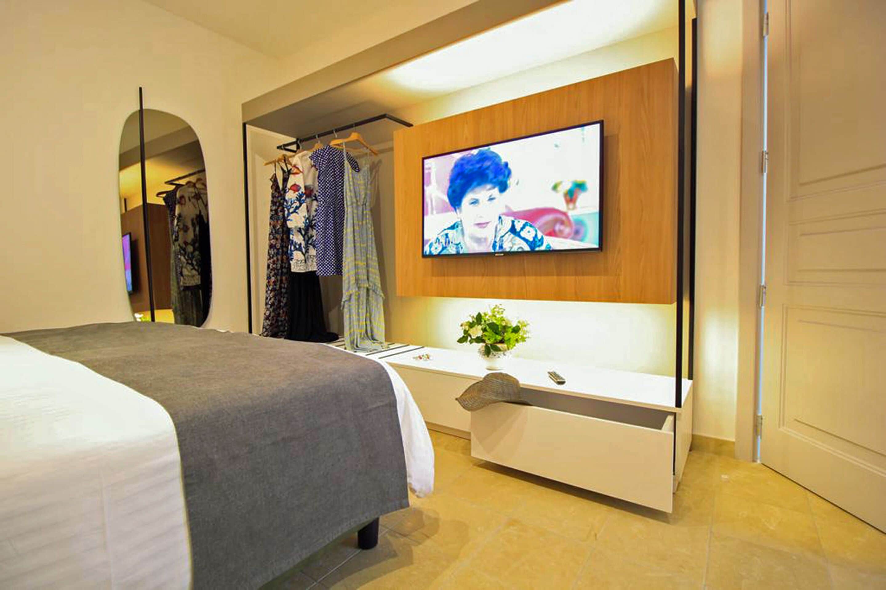 Una habitación de hotel moderna con una cama, un televisor montado en la pared, un tocador con espejo y un perchero.