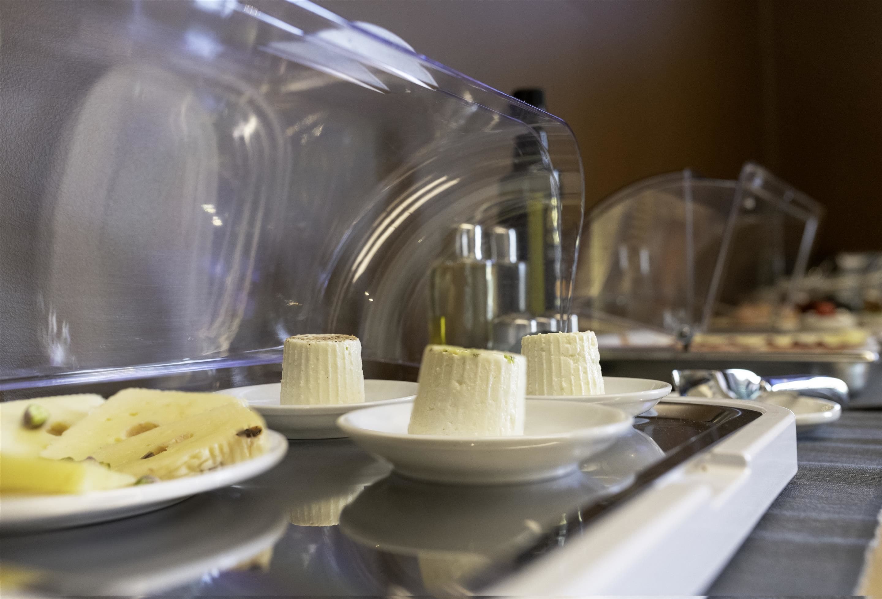 Un buffet avec des présentoirs de nourriture couverts, comprenant des desserts blancs et une assiette de fruits coupés.