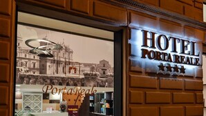 A hotel entrance with a sign reading "HOTEL PORTA REALE" and a view of the interior lobby with seating and a reception desk.
