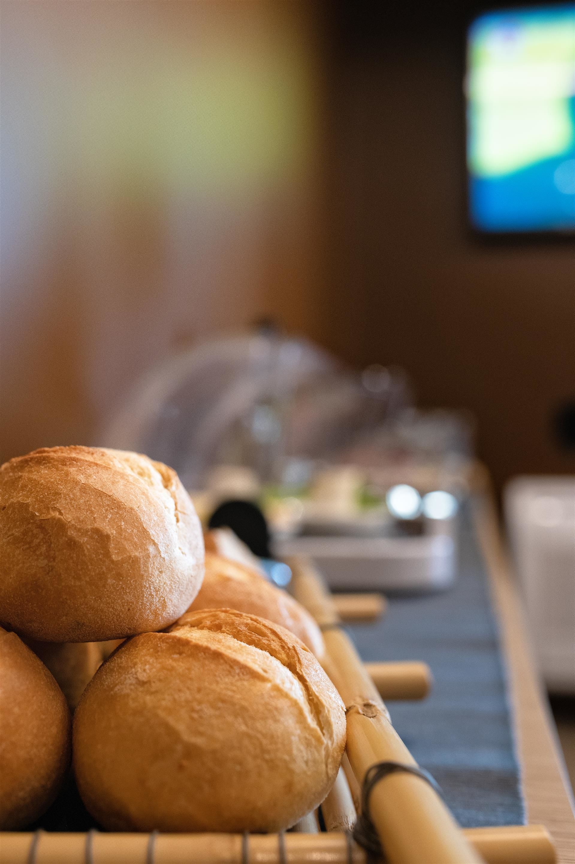A stack of round, golden-brown bread rolls on a bamboo tray.