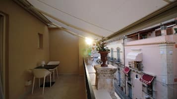 A narrow corridor with a table and chairs, a potted plant, and a balcony with a railing.