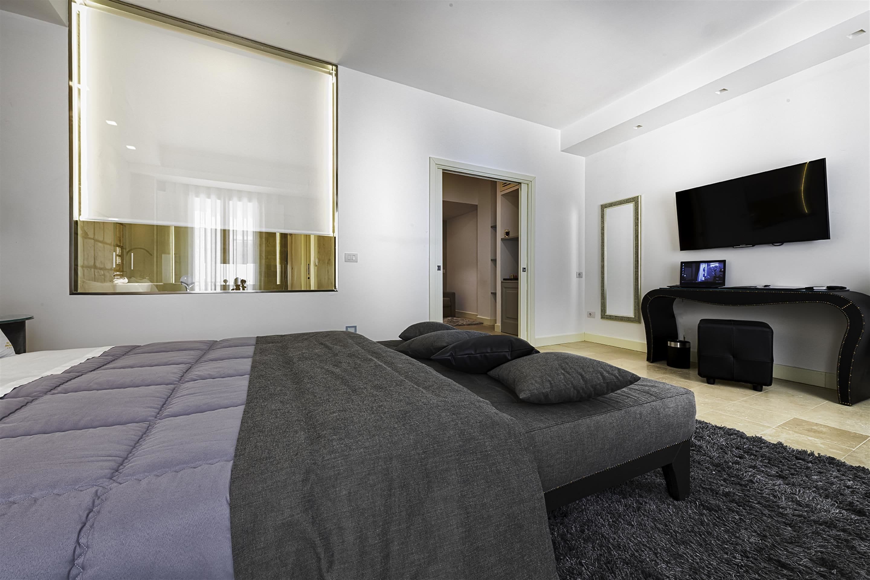 Ein modernes Schlafzimmer mit einem großen Bett, einem Schreibtisch, einem Fernseher und einem begehbaren Kleiderschrank.