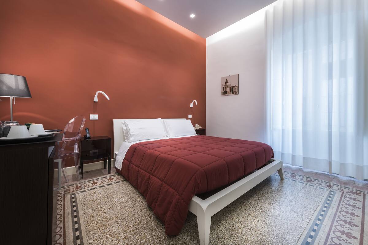 A bedroom with a bed, a desk, a chair, and a nightstand.