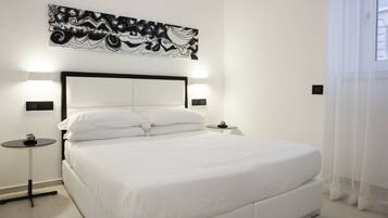 Une chambre d’hôtel moderne dotée d’un grand lit, d’une tête de lit avec éclairage intégré, d’une petite table de chevet et d’une œuvre d’art abstraite accrochée au mur.