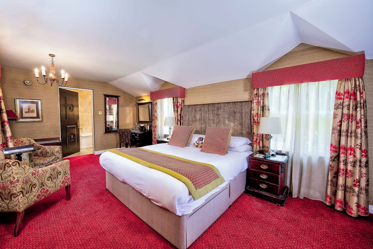 A hotel room with a large bed, a desk, a chair, a chandelier, and a window with curtains.