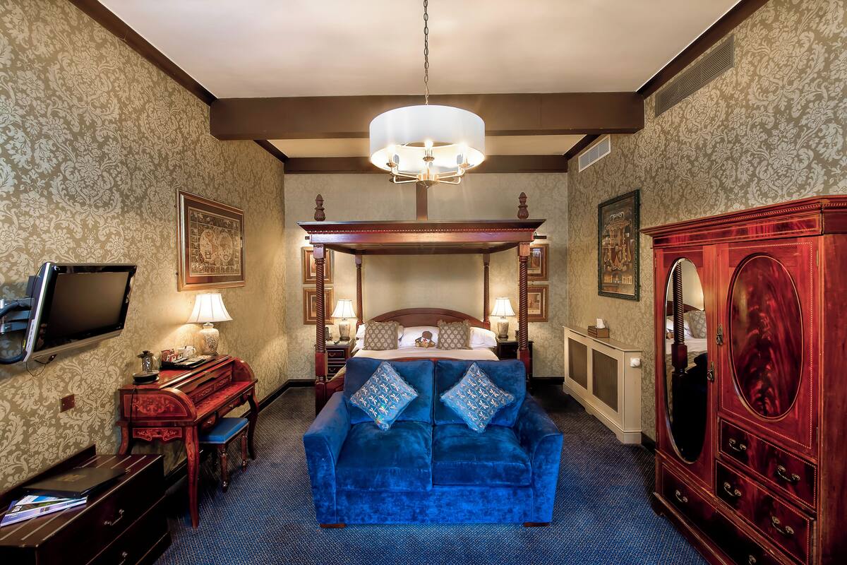 A hotel room with a large bed, a blue sofa, a wooden desk, a television, and a mirror.