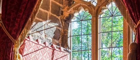 A room with a stone ceiling, large windows, and red curtains.