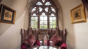 A room with a round table, two chairs, a bottle, and a stained glass window.
