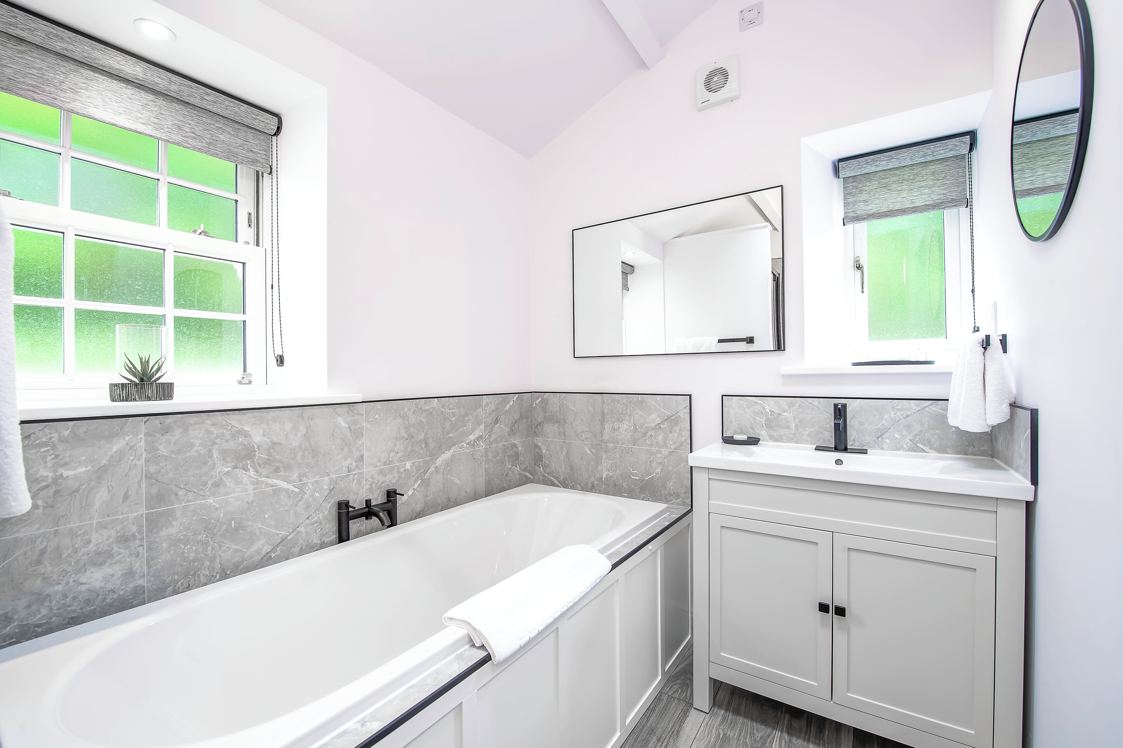 A modern bathroom with a freestanding bathtub, a vanity with a mirror, and a window with a view of greenery.