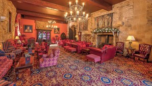 Una sala amplia con muebles tapizados en rojo, un candelabro y una pared de piedra con un mural.