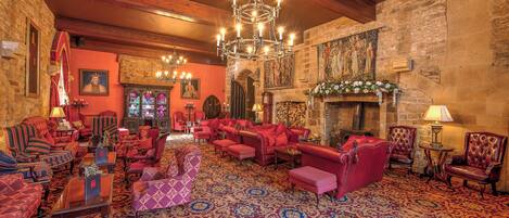 Una sala amplia con muebles tapizados en rojo, un candelabro y una pared de piedra con un mural.