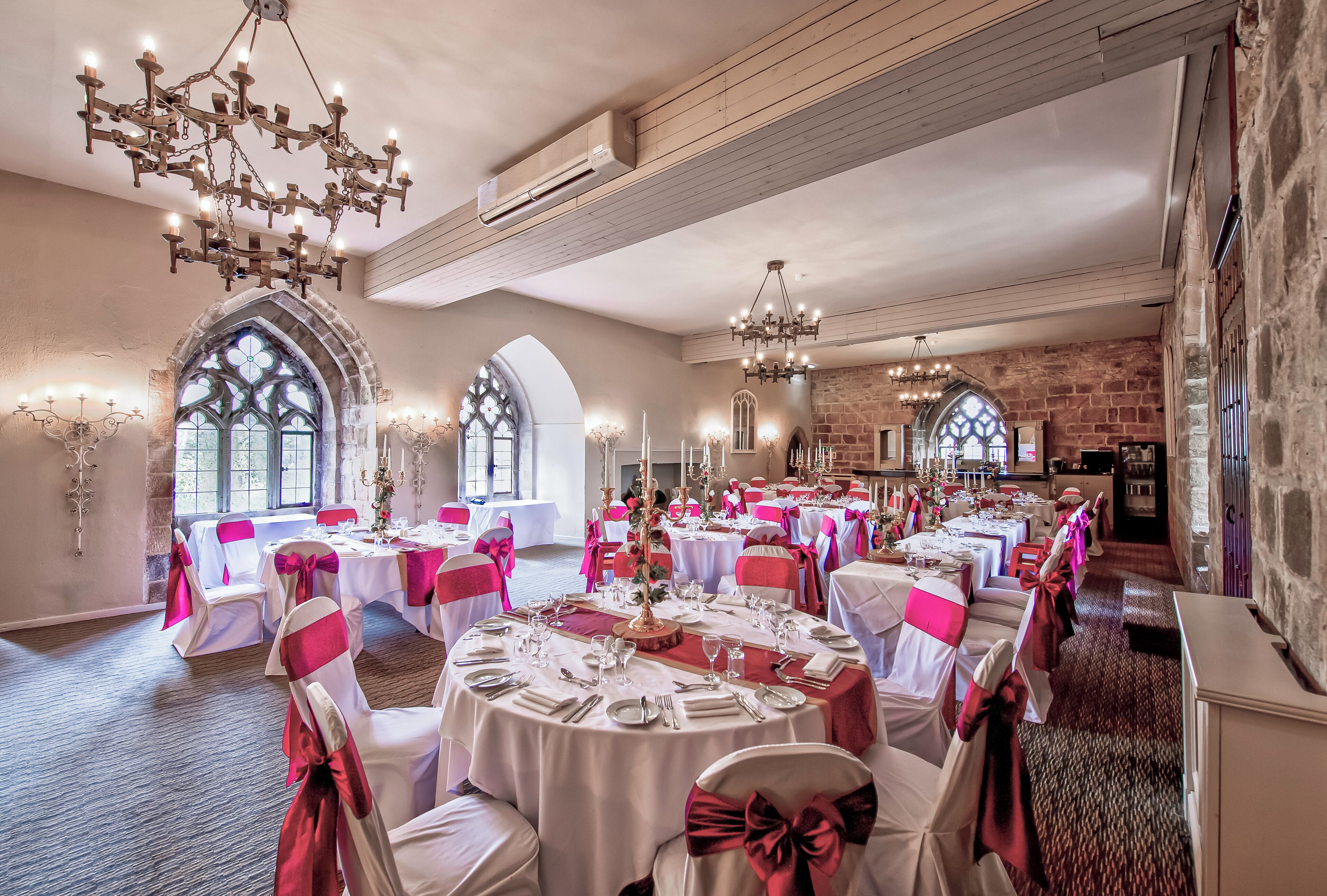 A banquet hall with round tables, white tablecloths, and chairs with pink sashes.