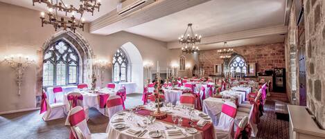 A banquet hall with round tables, white tablecloths, and chairs with pink sashes.