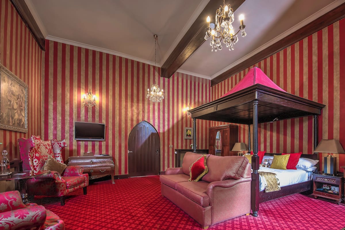 A room with a four-poster bed, a chaise lounge, a television, and a chandelier.