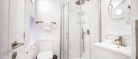 Un baño moderno con ducha de vidrio, inodoro y lavamanos con espejo.