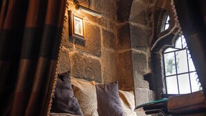 Habitación con paredes de piedra, una cama, un cuadro enmarcado y una ventana.