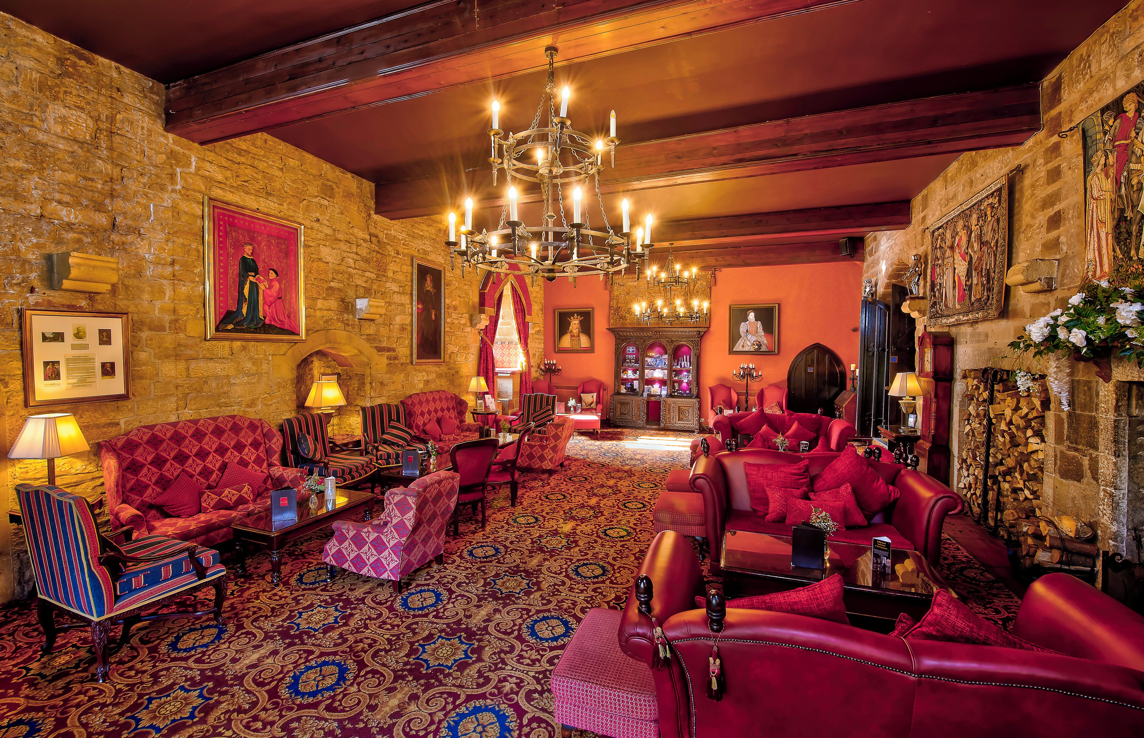 A luxurious room with red leather sofas, a chandelier, and a stone wall with artwork.