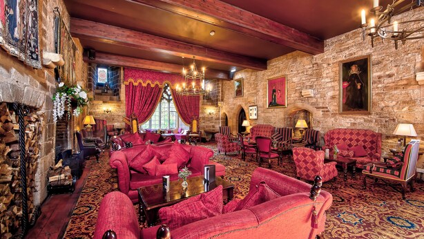 Una habitación tradicional con paredes de piedra, muebles tapizados en rojo y un candelabro.