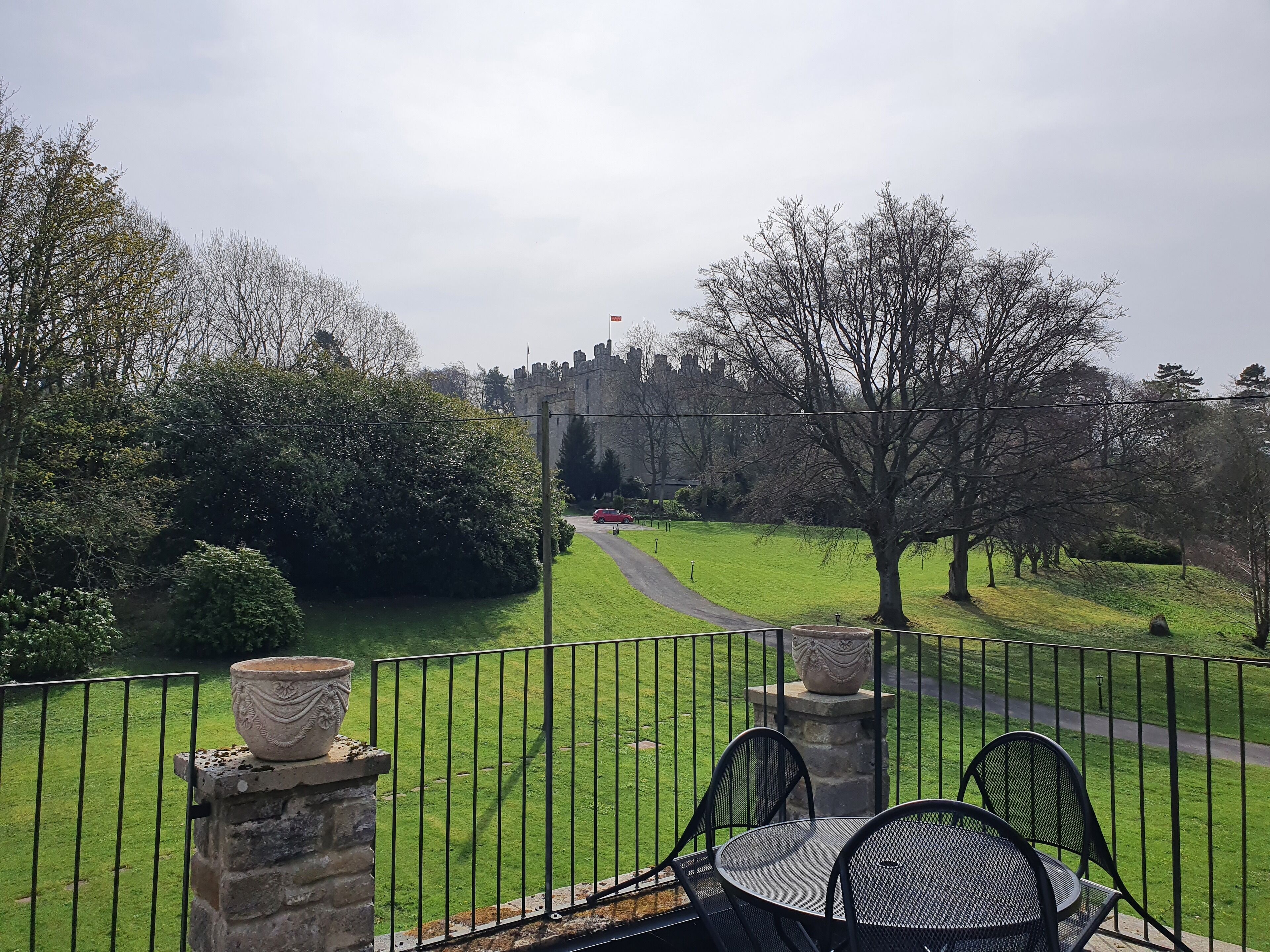 A balcony with a view of a castle, a paved path, and a grassy area.