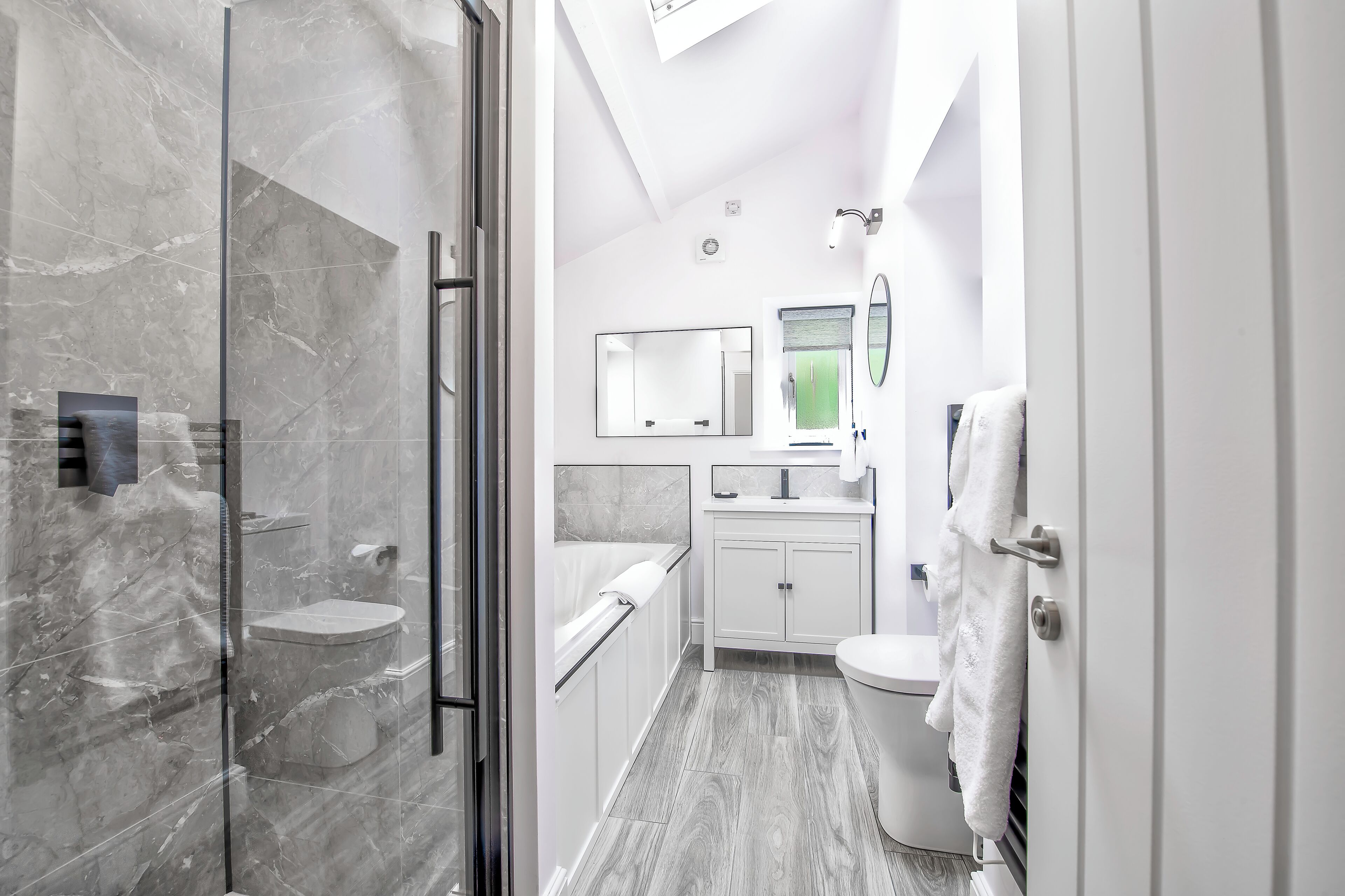 A modern bathroom with a glass shower enclosure, a white toilet, a sink with a mirror, and a towel hanging on the wall.