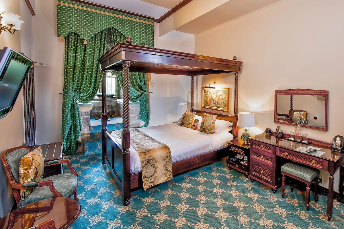 A four-poster bed with a wooden frame, a desk with a mirror, and a chair with a cushion.