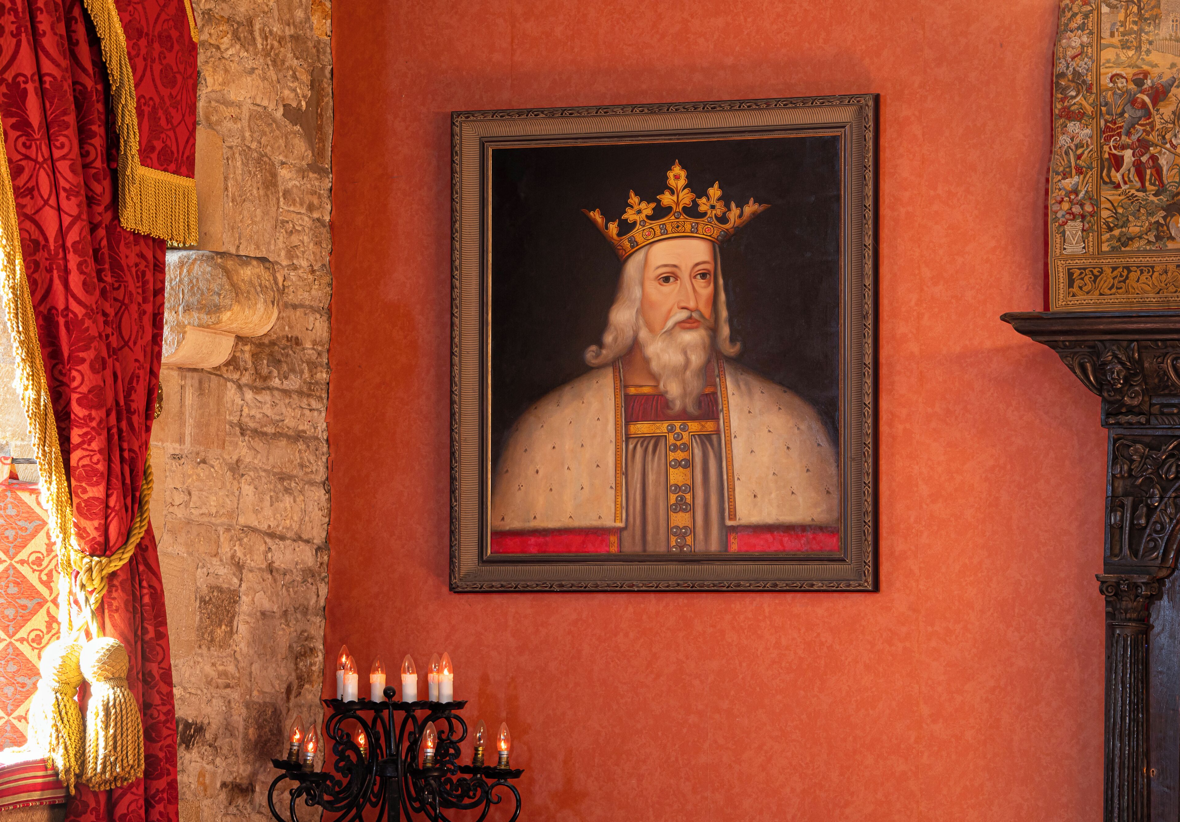 Un retrato de una figura histórica en un cuadro enmarcado en la pared, un candelabro con velas encendidas y una cortina roja con flecos.