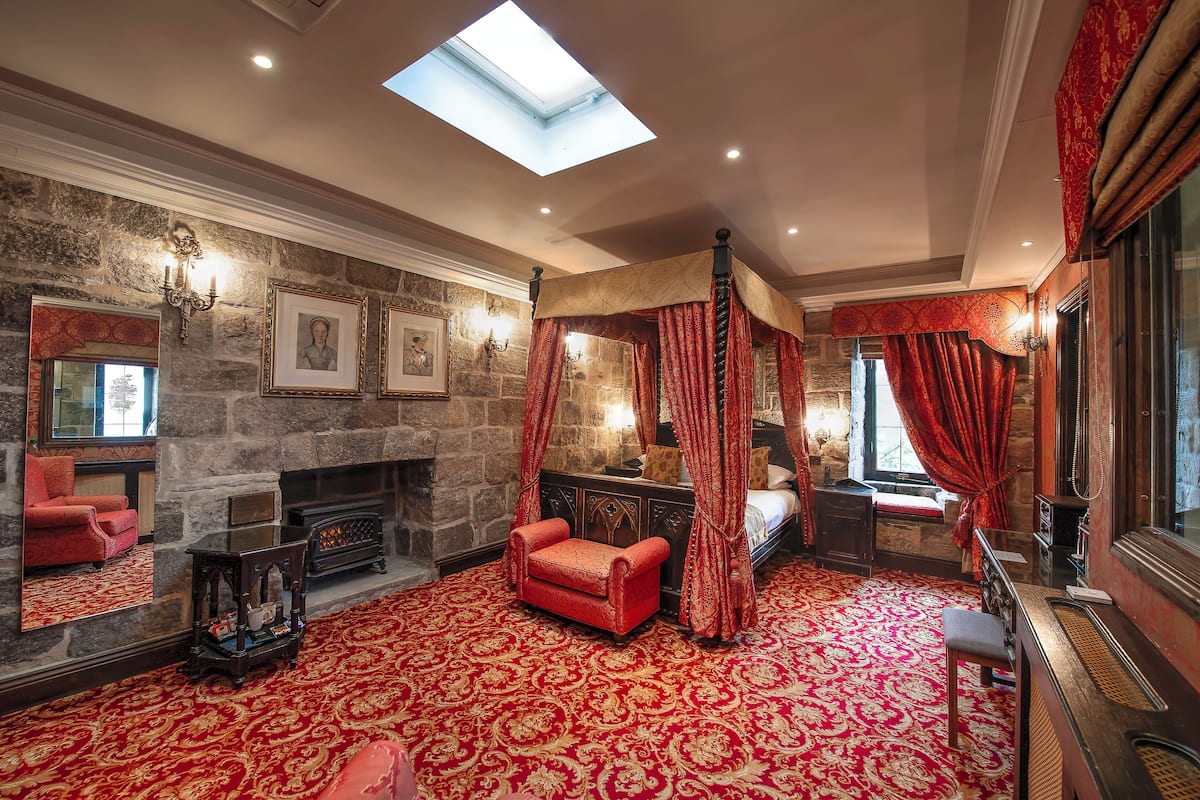 A room with a stone fireplace, a four-poster bed, and a red carpet.