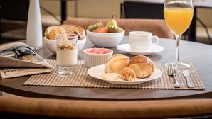 Una mesa de desayuno con cruasanes, un vaso de jugo de naranja y un bol de fruta.