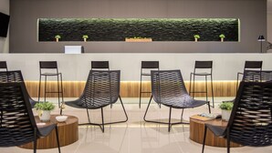 Un área de recepción con diseño moderno, que incluye un mostrador de recepción, varias sillas negras, una mesa de centro de madera y un jarrón de planta en la pared.