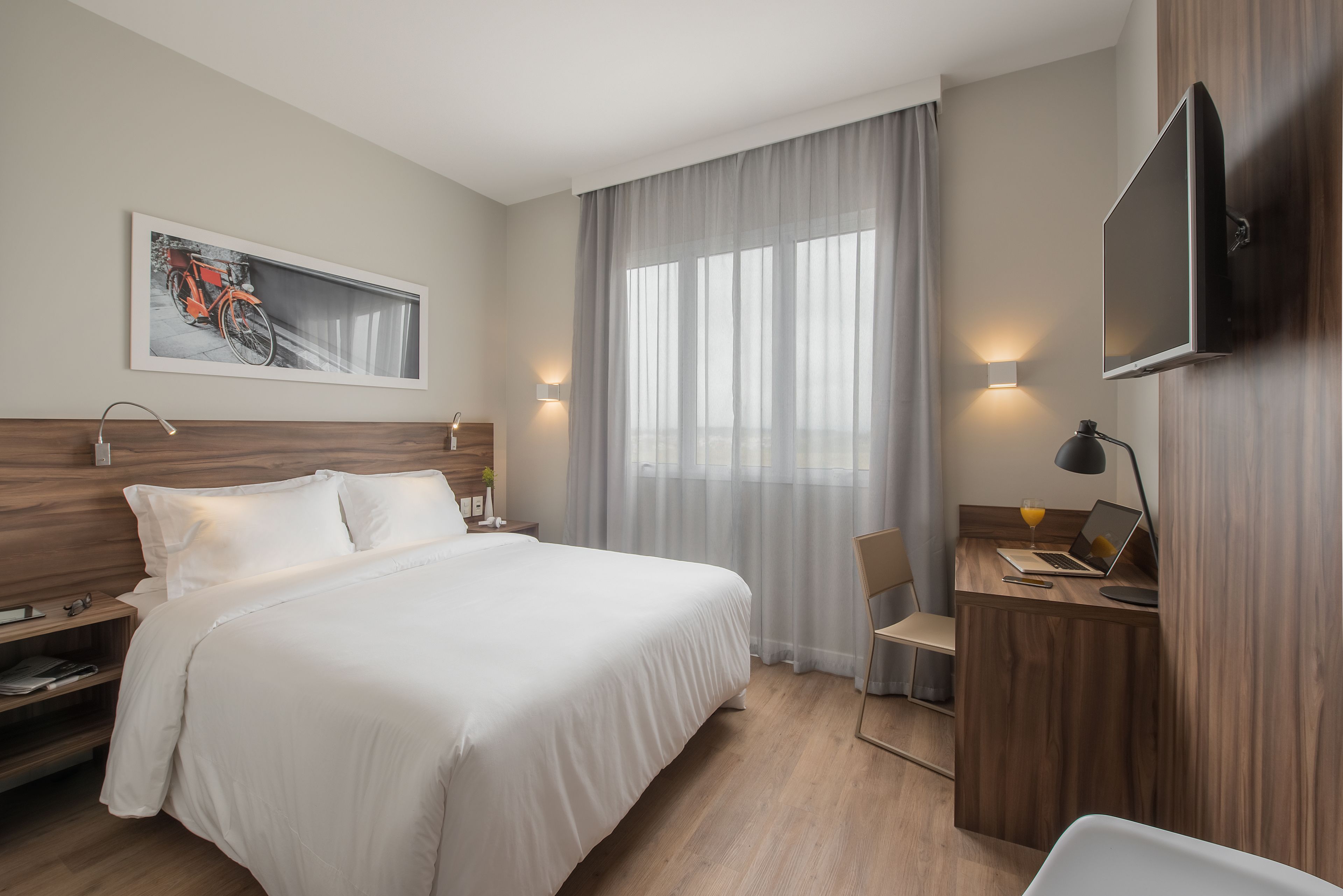 Una habitación de hotel con cama, escritorio, silla y televisión en la pared.