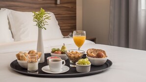Una bandeja de desayuno ordenada sobre la cama, con una almohada blanca, un florero con una planta y un vaso de jugo de naranja.