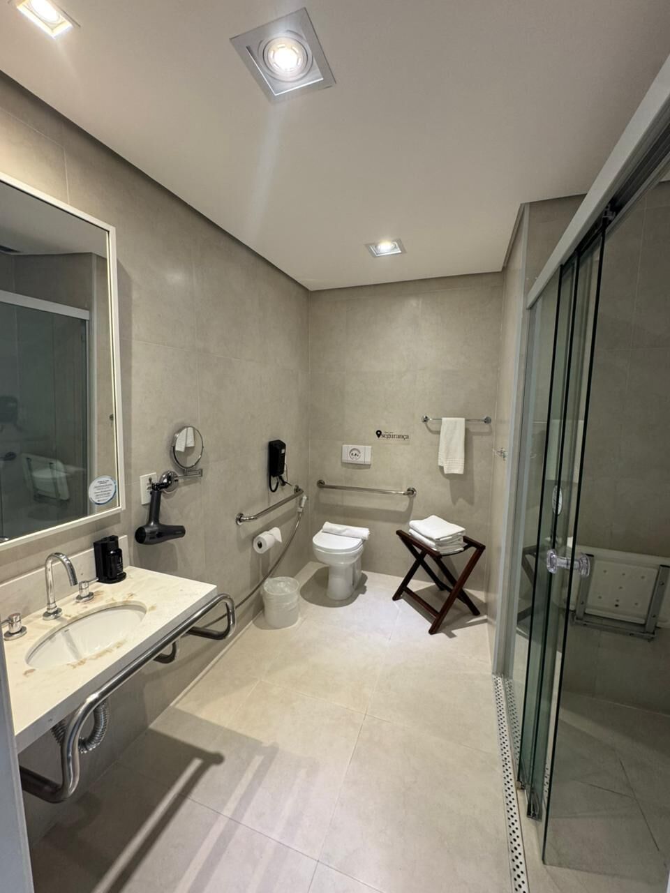 A modern bathroom with a large mirror, a sink, a toilet, and a glass shower enclosure.