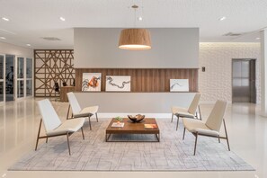 A modern lobby with a central coffee table, two white chairs, a wooden partition with artwork, and a ceiling light. - Intercity Pátio Pinda Hotel & Resort (Pindamonhangaba)