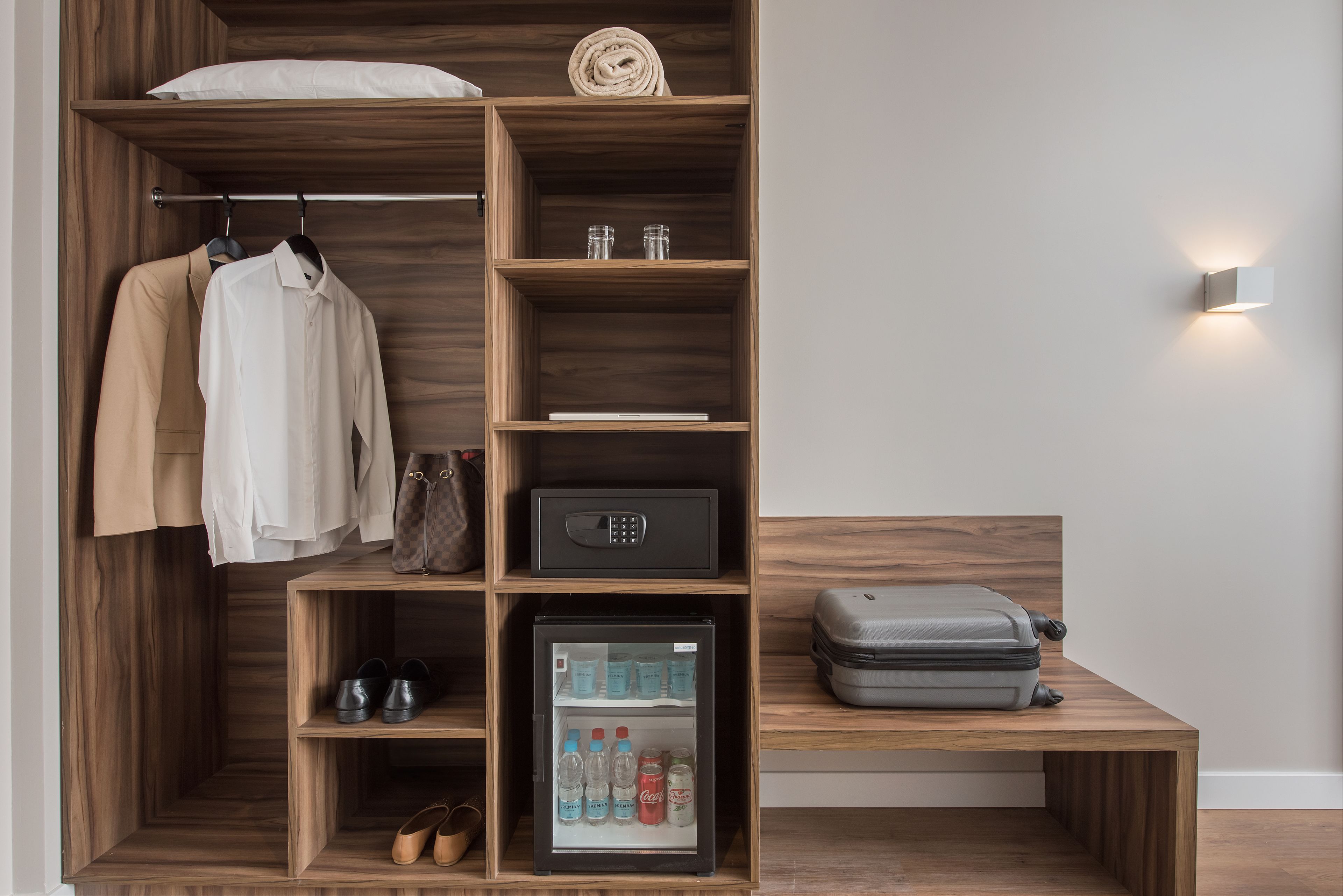 A compact room with a wardrobe, a small refrigerator, and a table with a suitcase.