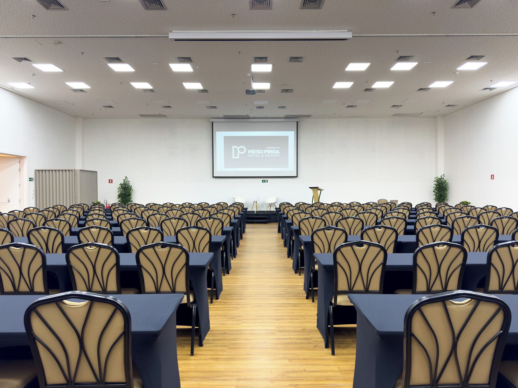 Un salón de conferencias con filas de sillas y una pantalla de proyector mostrando una presentación.