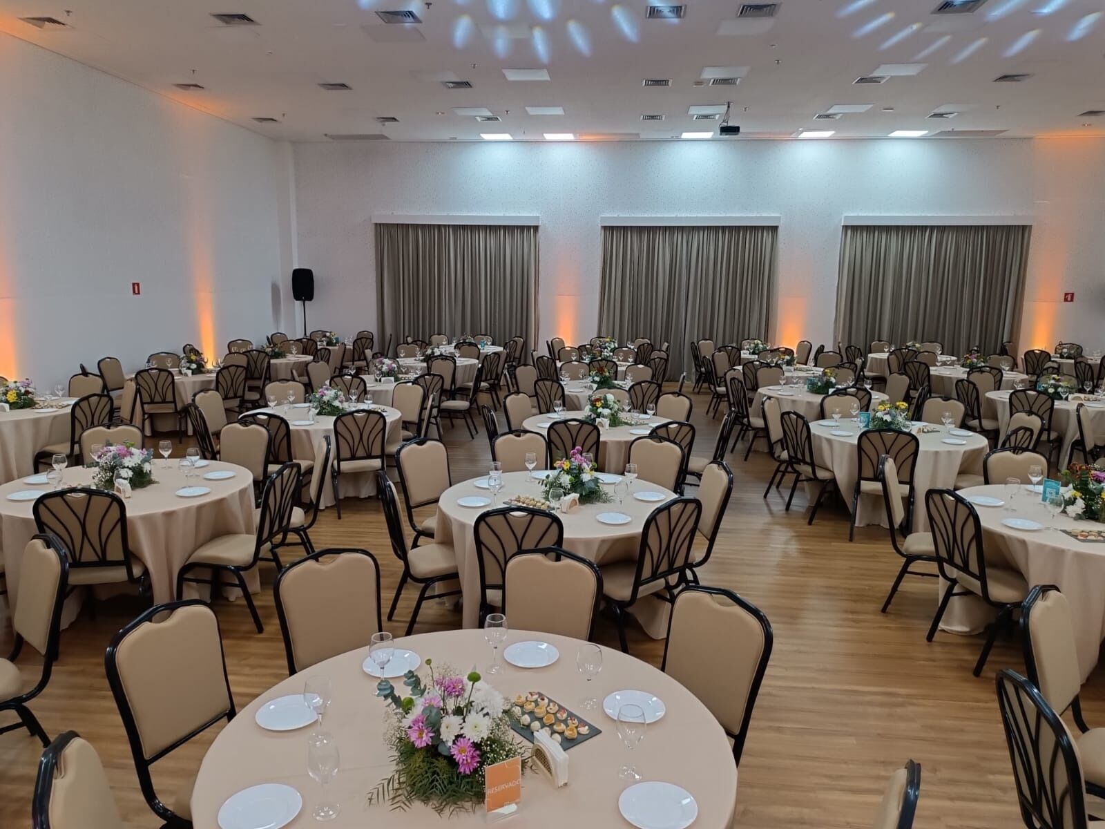 Une salle de banquet avec des tables rondes, des chaises et des rideaux.