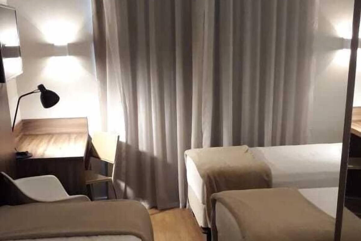 A hotel room with two beds, a desk, a chair, and a lamp.