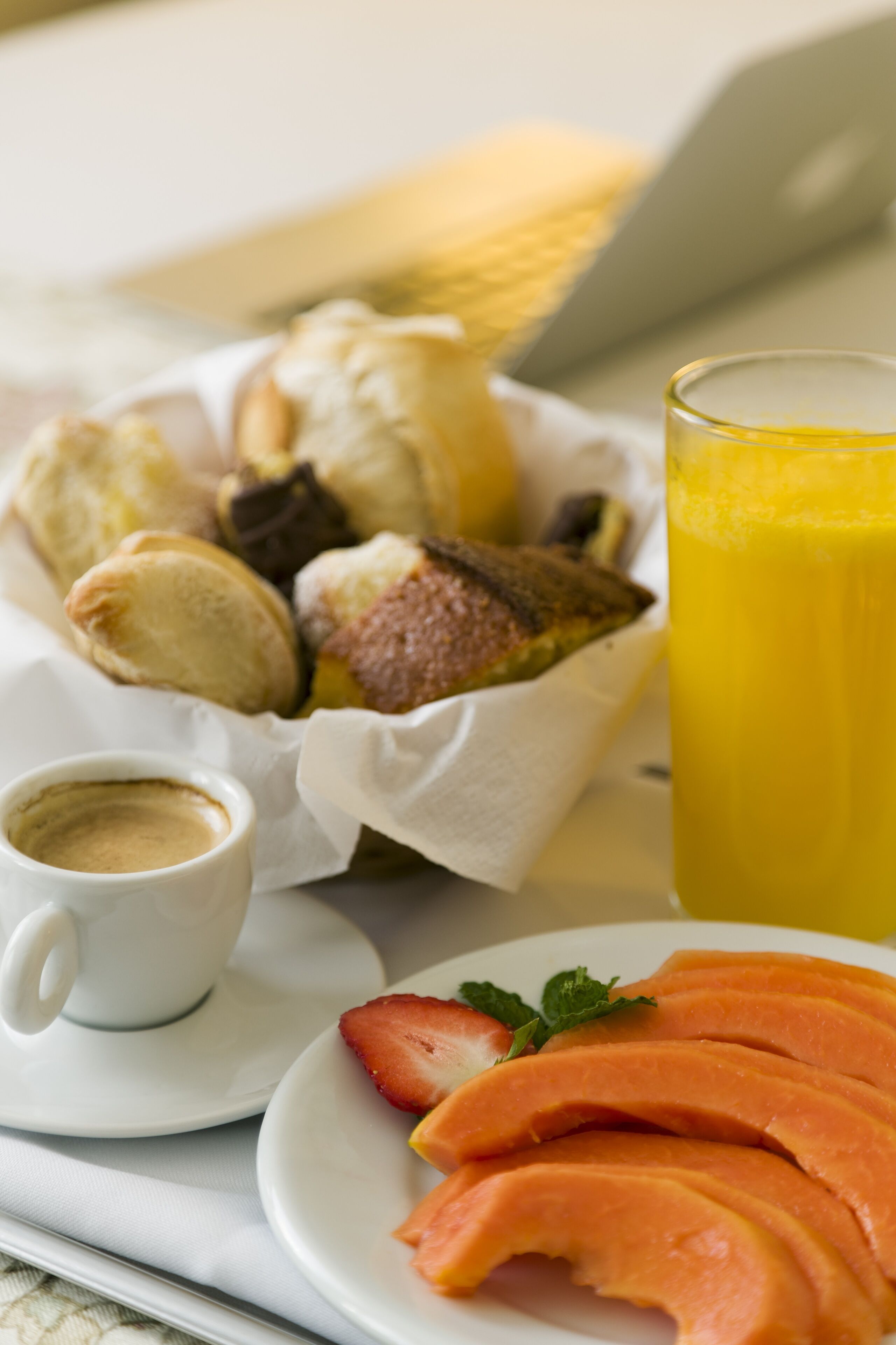 A breakfast tray with pastries, a glass of orange juice, a cup of coffee, and sliced fruit.