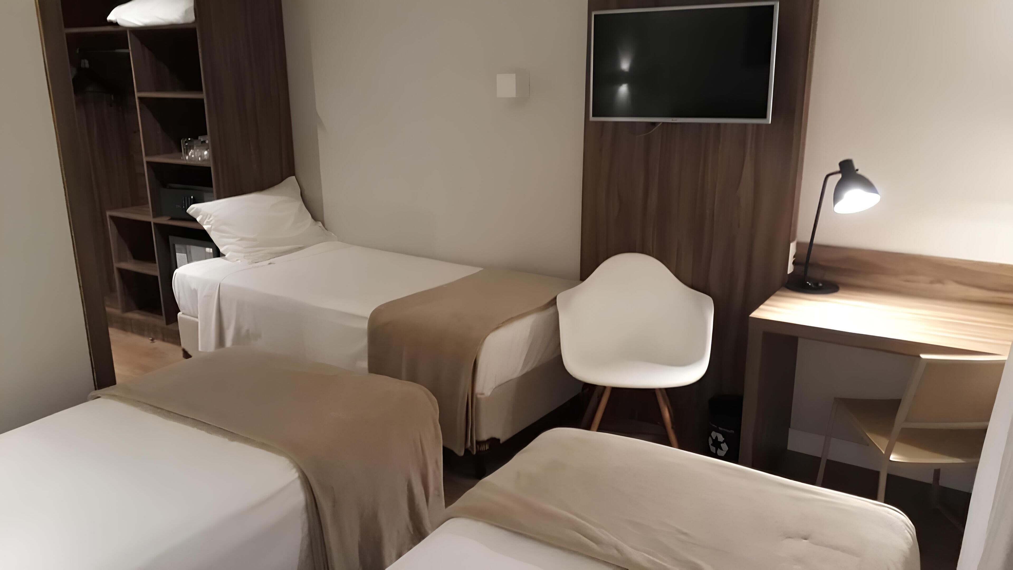 A hotel room with two beds, a desk, a chair, a TV, and a wardrobe.