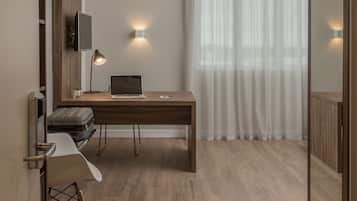 Quarto de hotel moderno com uma escrivaninha de madeira, um laptop, uma cadeira, uma mala e um espelho grande.
