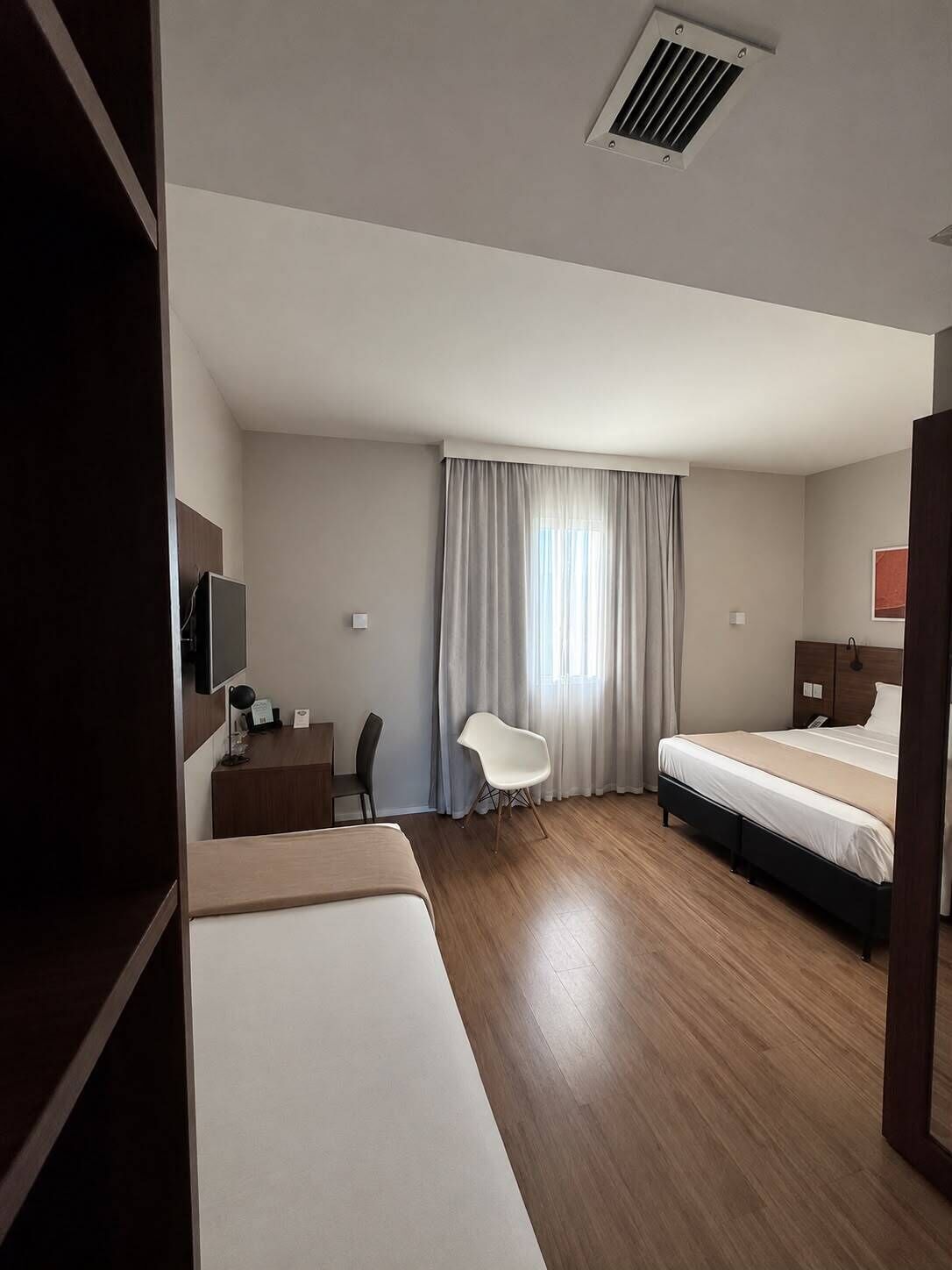 A hotel room with a bed, a desk, a chair, and a television.
