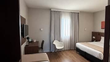A hotel room with a bed, a desk, a chair, and a television.