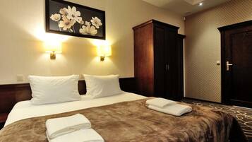 A hotel room with a large bed, two wall-mounted lamps, a framed floral artwork, a wardrobe, and a carpeted floor.
